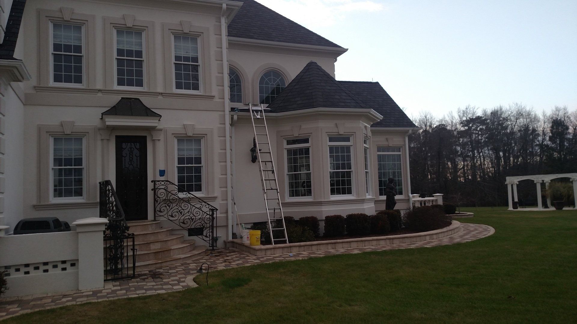 Large beige house with white trim, stone accents, and a curved lawn under a bright sky