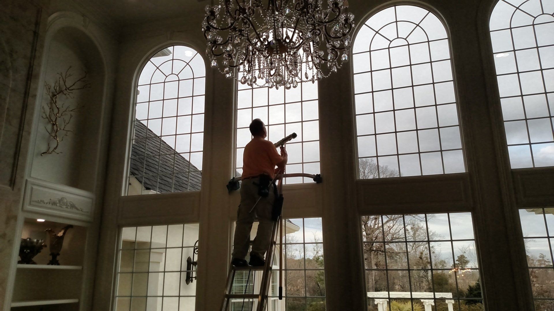 Person on a ladder painting tall arched windows in a bright room