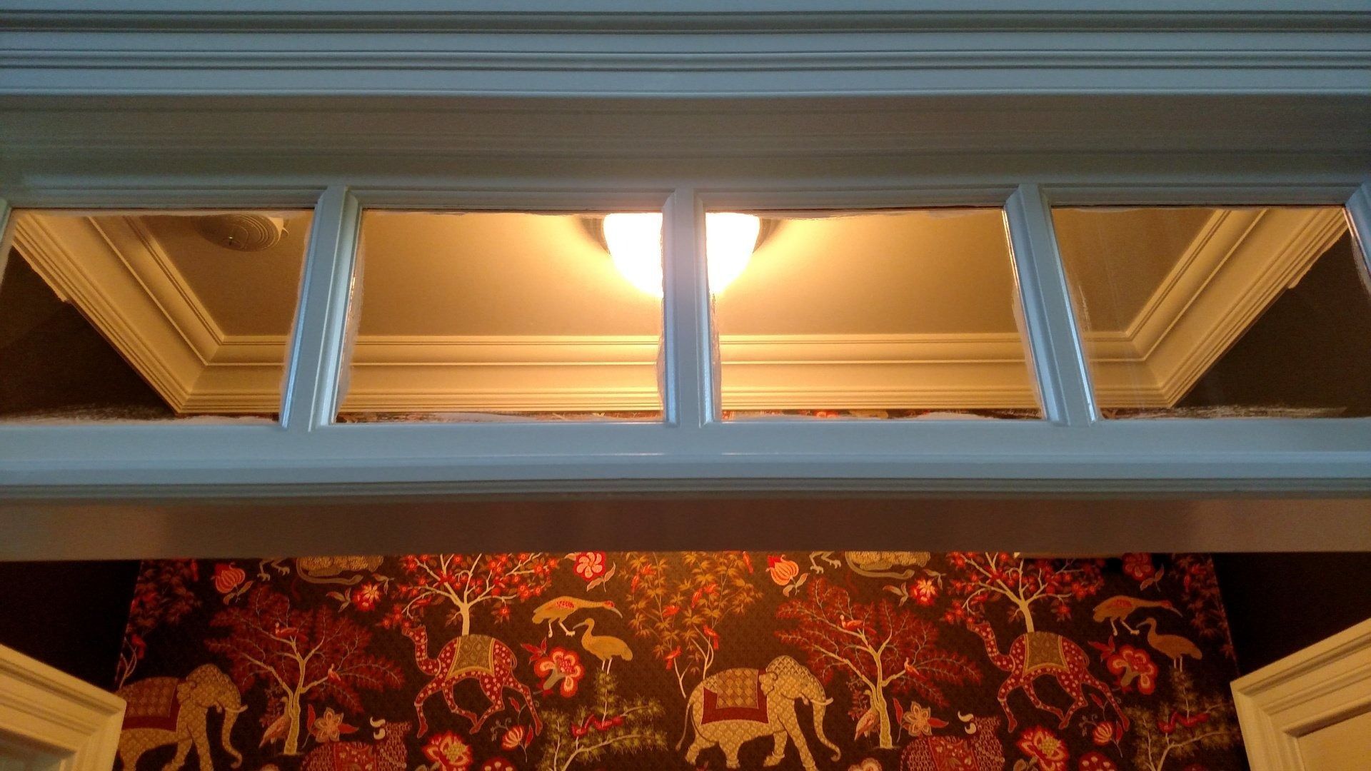 Blue-framed transom windows above a red patterned wall covering, lit warmly from inside