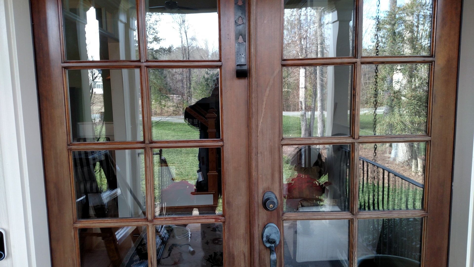 Wooden French doors with glass panes reflecting an outdoor deck and trees