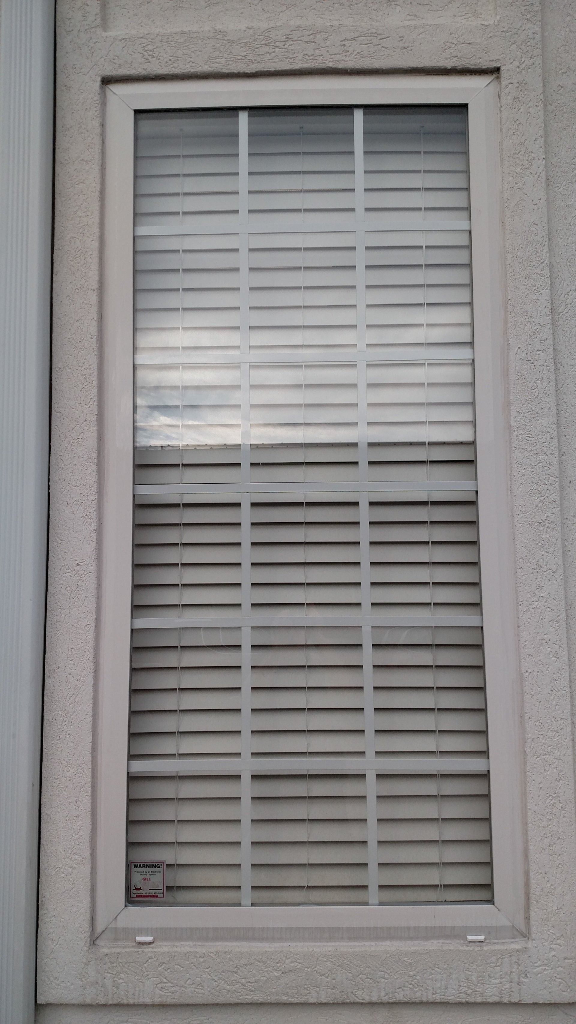 Closed window with white blinds and a textured beige frame on an exterior wall