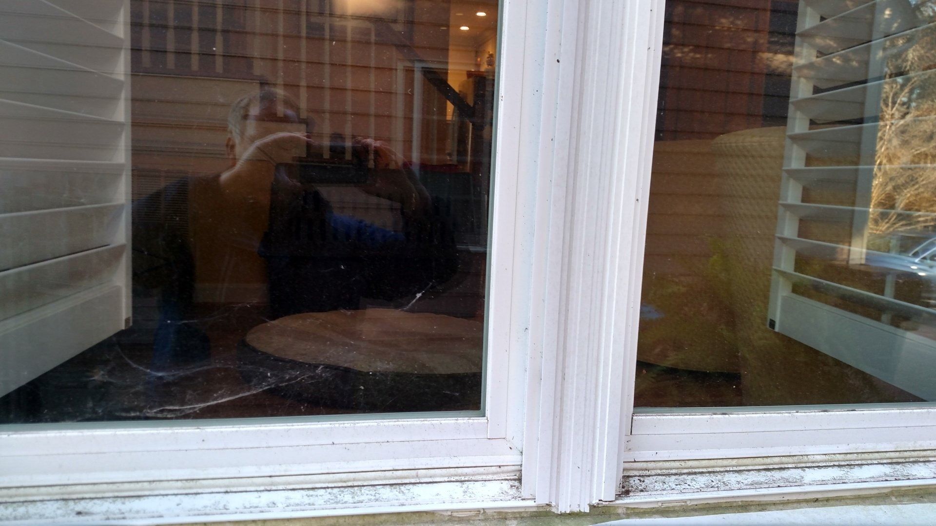 Window with white trim reflecting an indoor table and chair, with warm-lit room visible inside