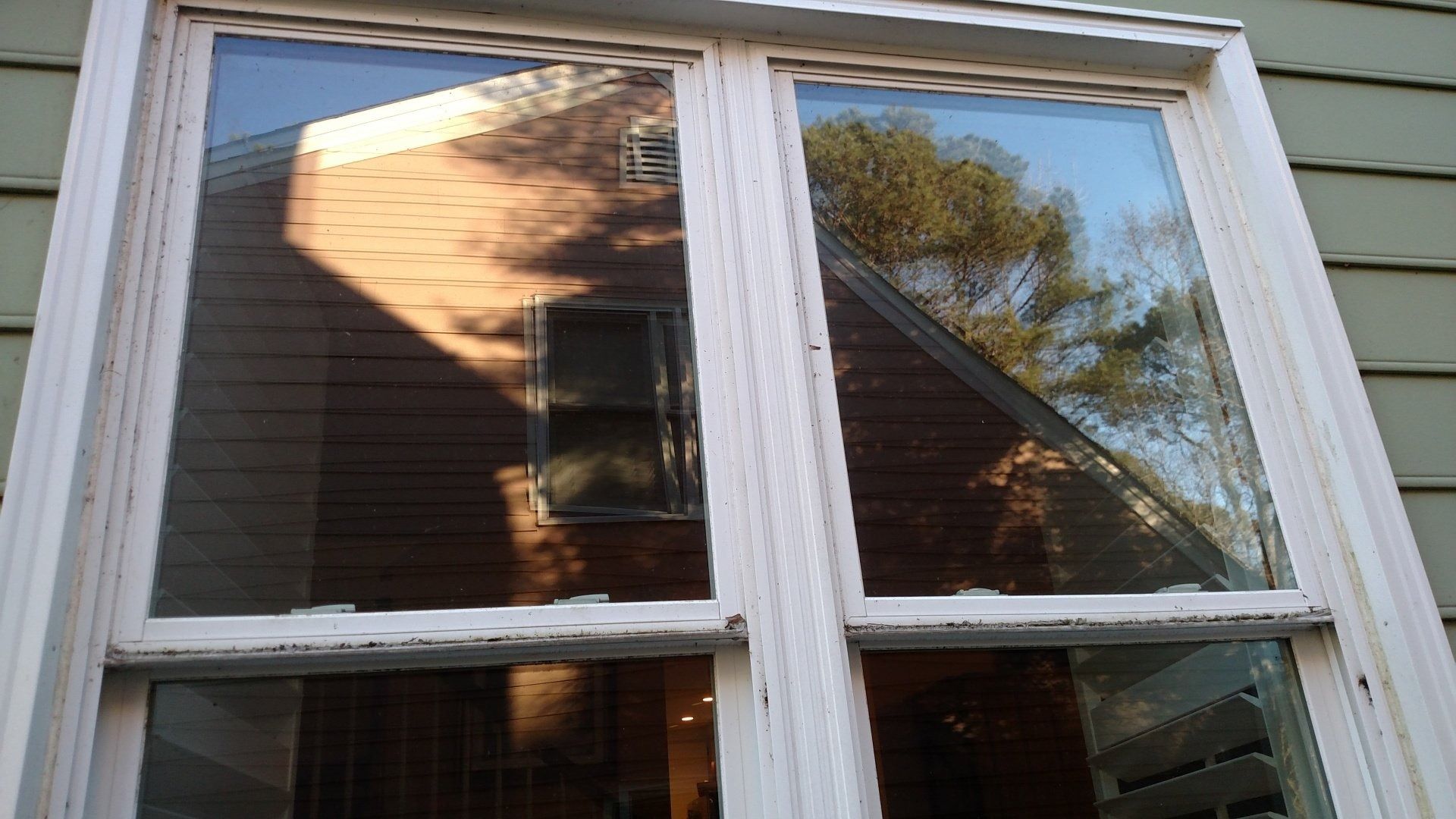 A window reflecting a brick house, trees, and sunlight, with white trim and two panes.