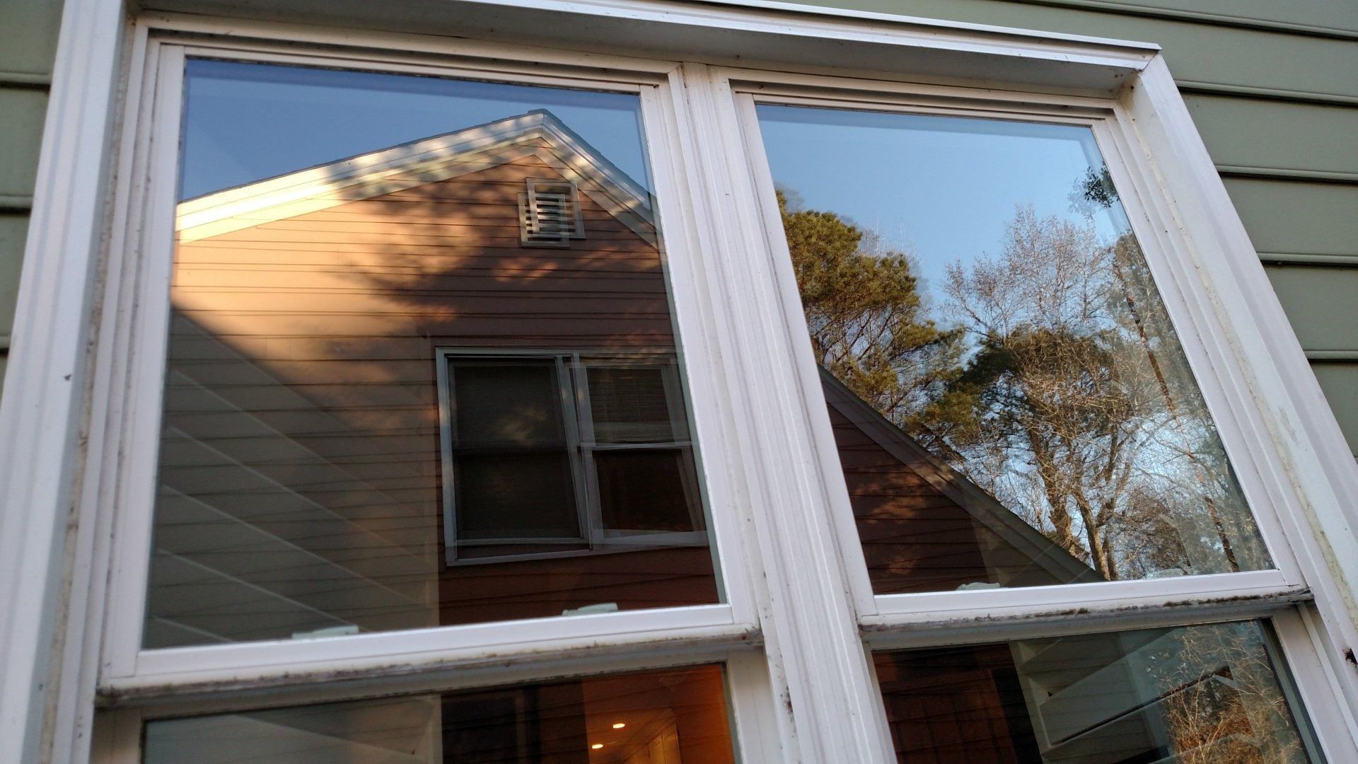 White-framed windows reflecting a house, tree, and warm sunlight on a beige exterior wall