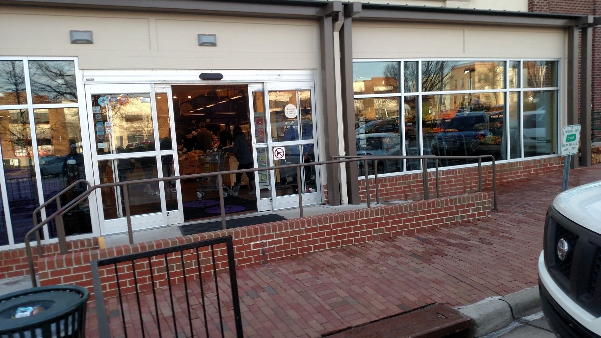 Storefront with large windows and glass doors, brick planter, and a parked vehicle at the curb.