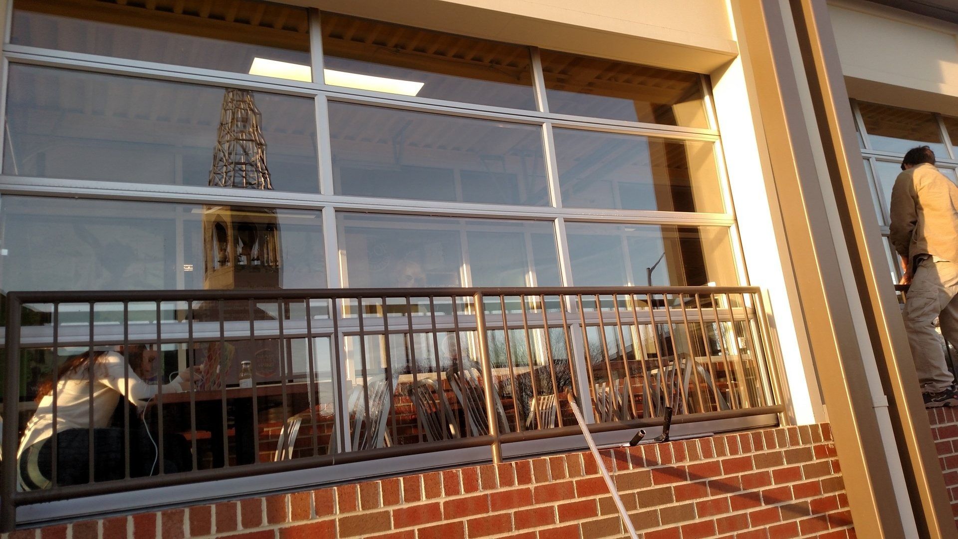 Brick storefront with large reflective windows and a person standing at the right edge of the frame