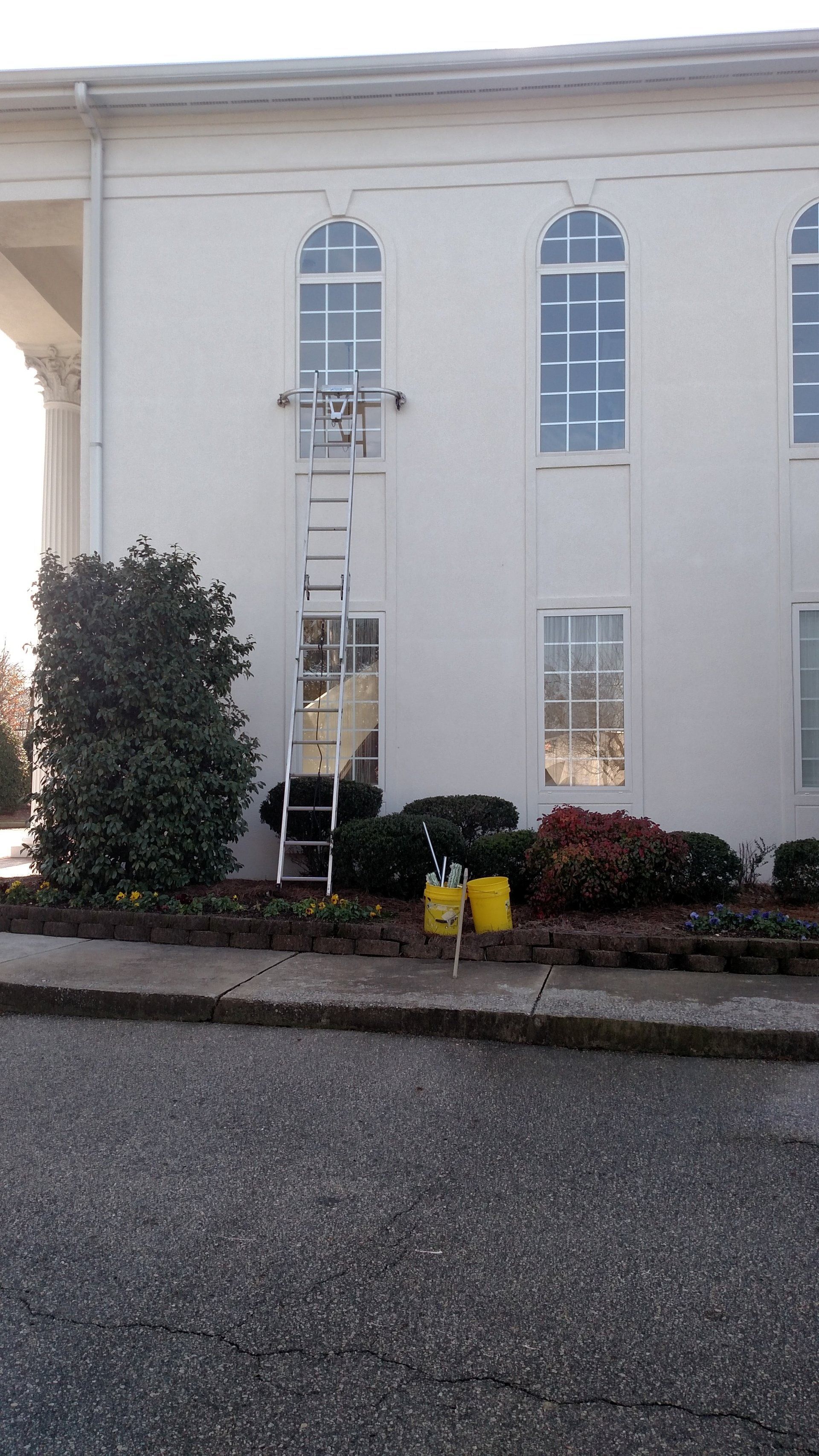 Beige two-story building with arched windows, shrubs, and yellow planters by the entrance.