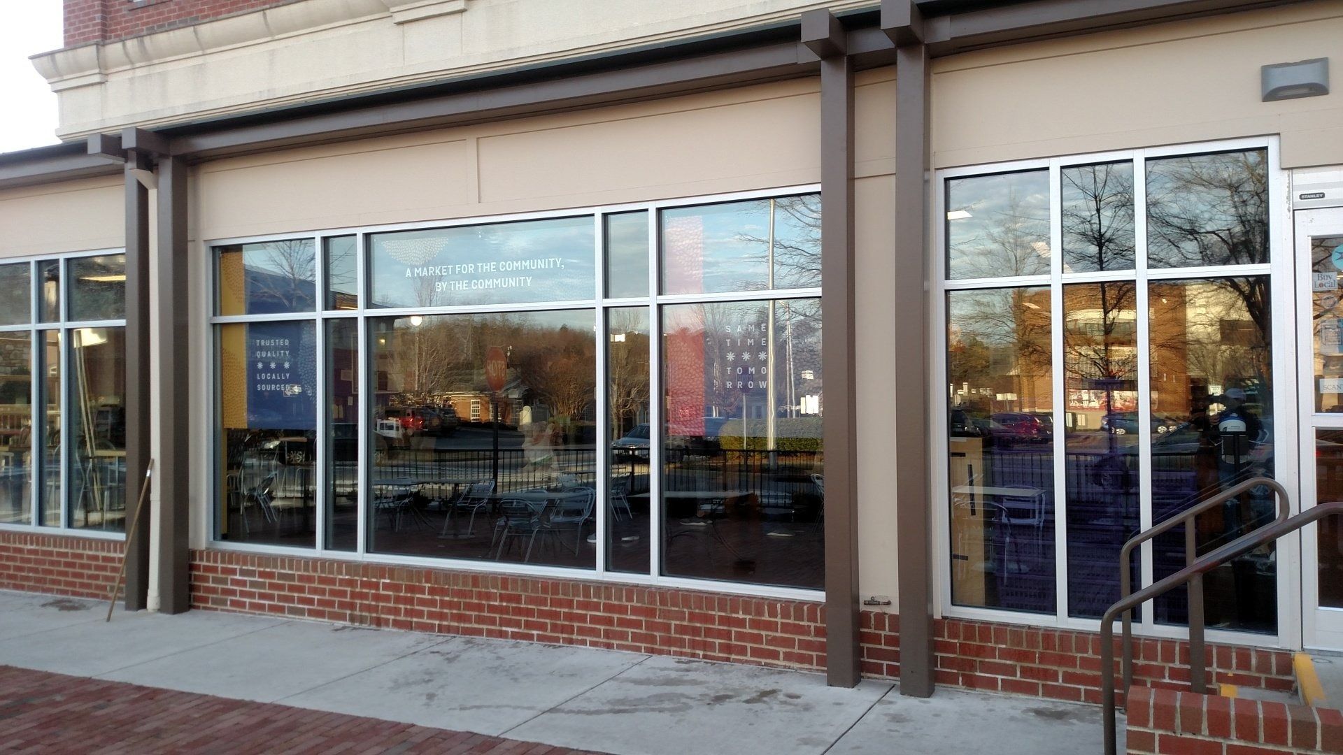 Storefront with large windows and a brick base, viewed from the sidewalk at dusk.