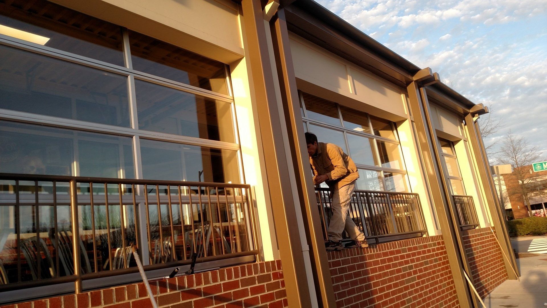 Person climbing through a window of a brick building with metal railings at sunset.
