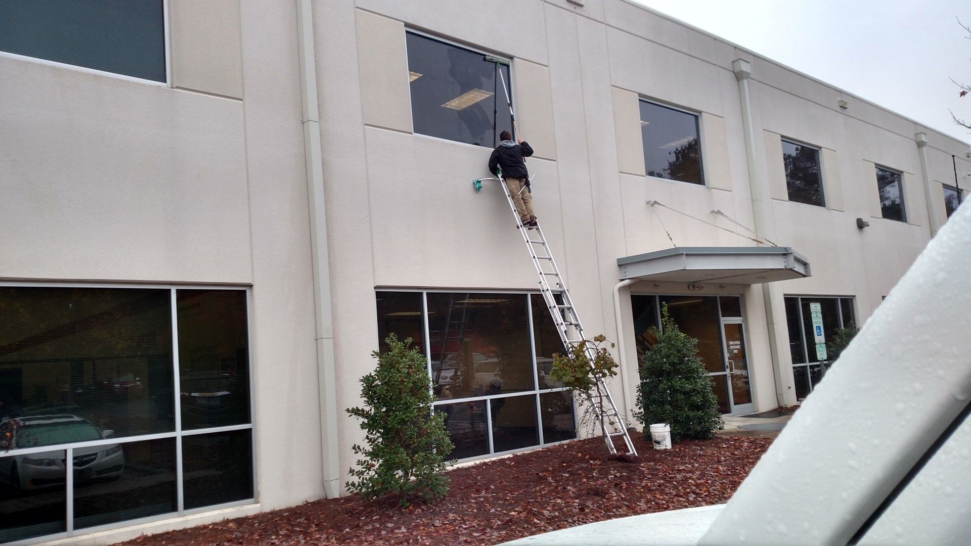Person on a ladder working on a second-story window of a beige building