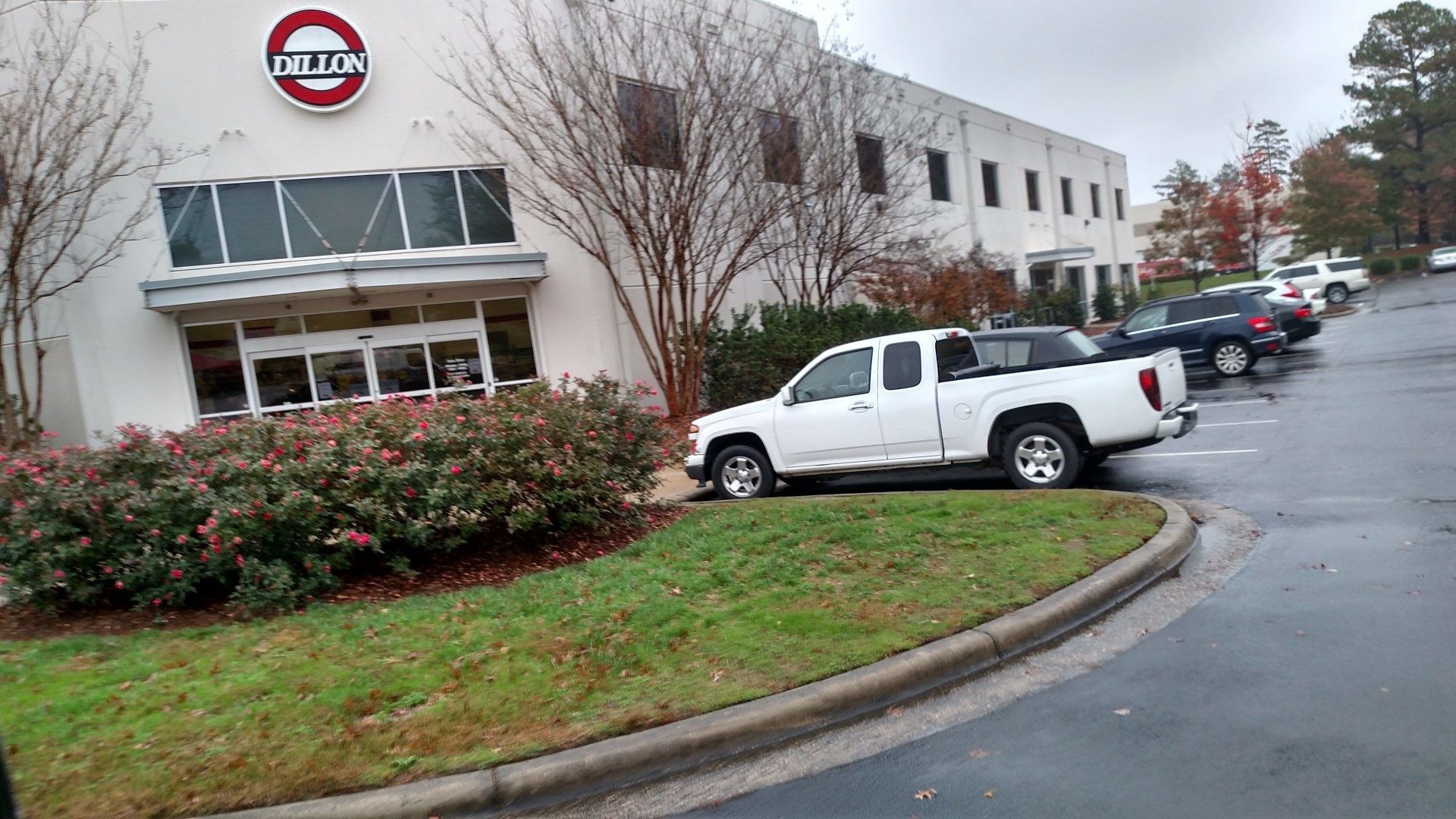 Parking lot outside a Nissan building on a rainy day, with several parked vehicles and shrubs in front.