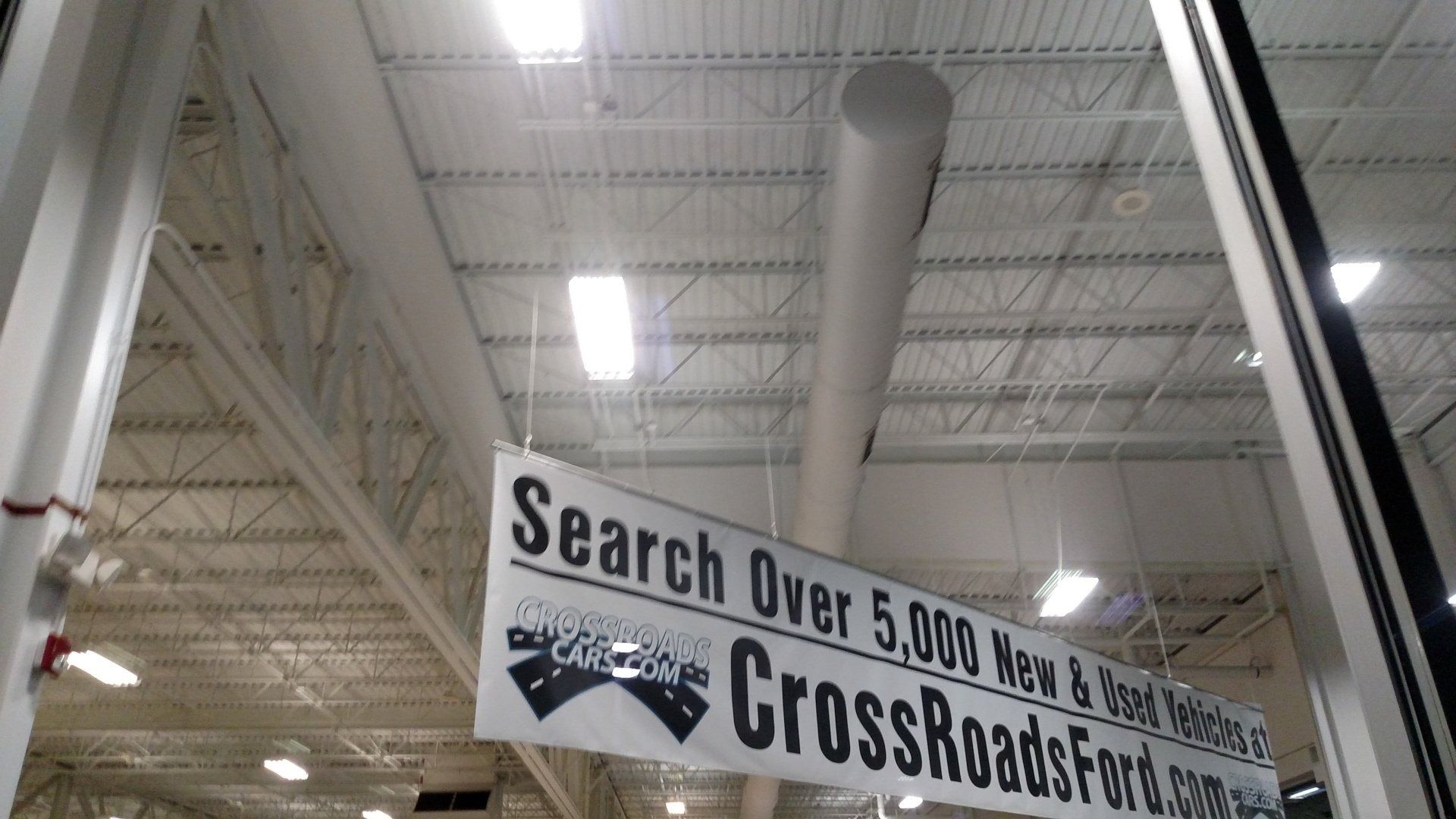Indoor warehouse aisle with a hanging banner reading “Search Over 5,000 New and Used Cars.”