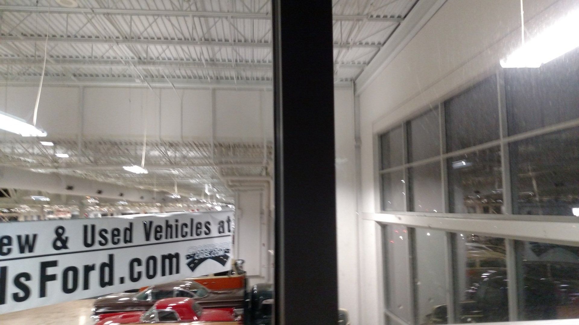 Car showroom interior with cars, large windows, and a “New & Used Vehicles” Ford sign.