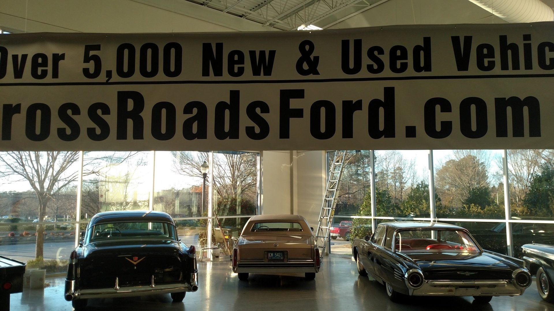 Used car showroom with three classic cars and a CrossRoadsFord.com banner above them