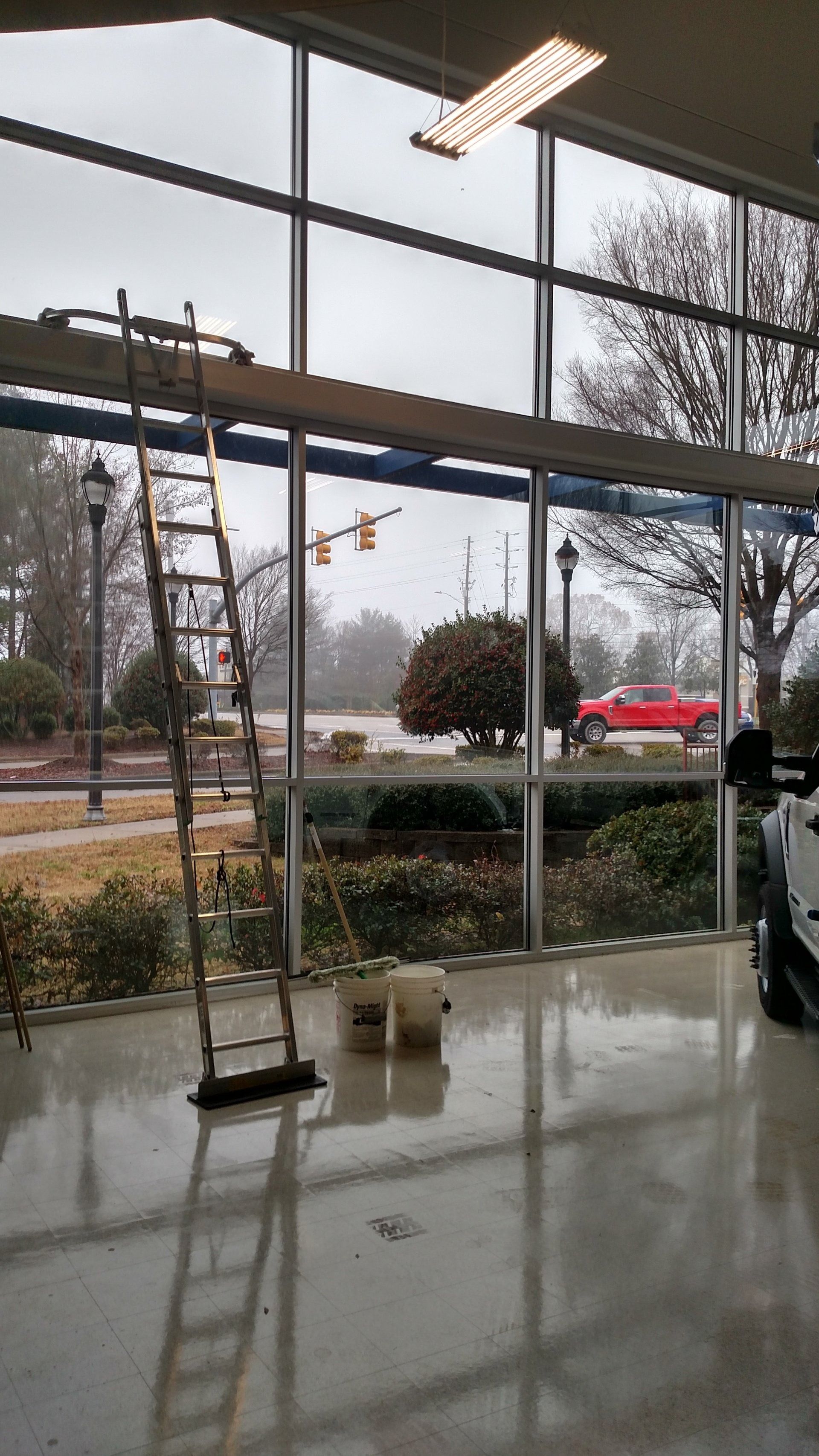 Rainy storefront with large glass windows, wet floor, and a tree-lined parking lot outside