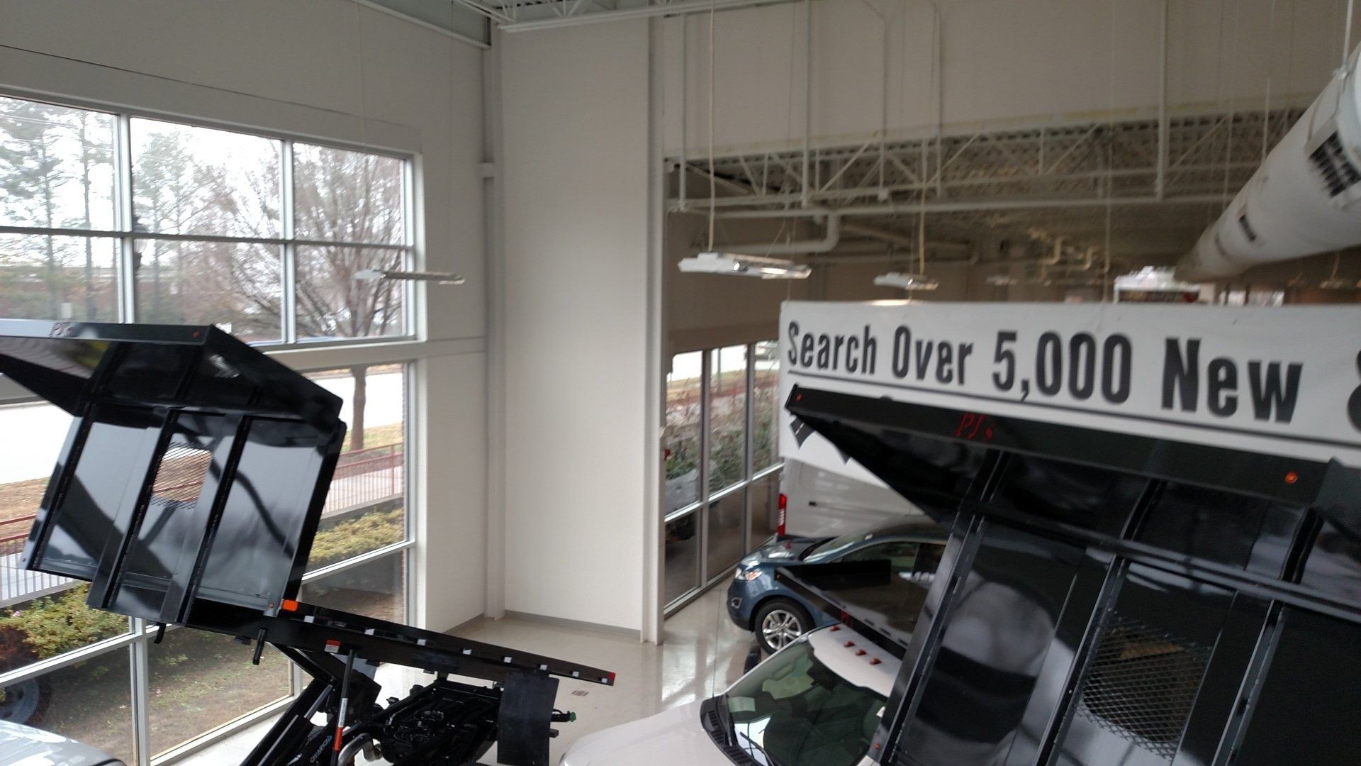 Indoor showroom with vehicles and a large banner reading “Search Over 5,000 New”