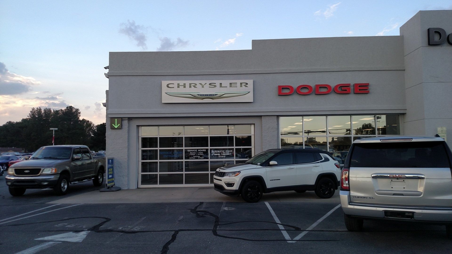 Car dealership storefront with Dodge sign and vehicles parked outside at dusk