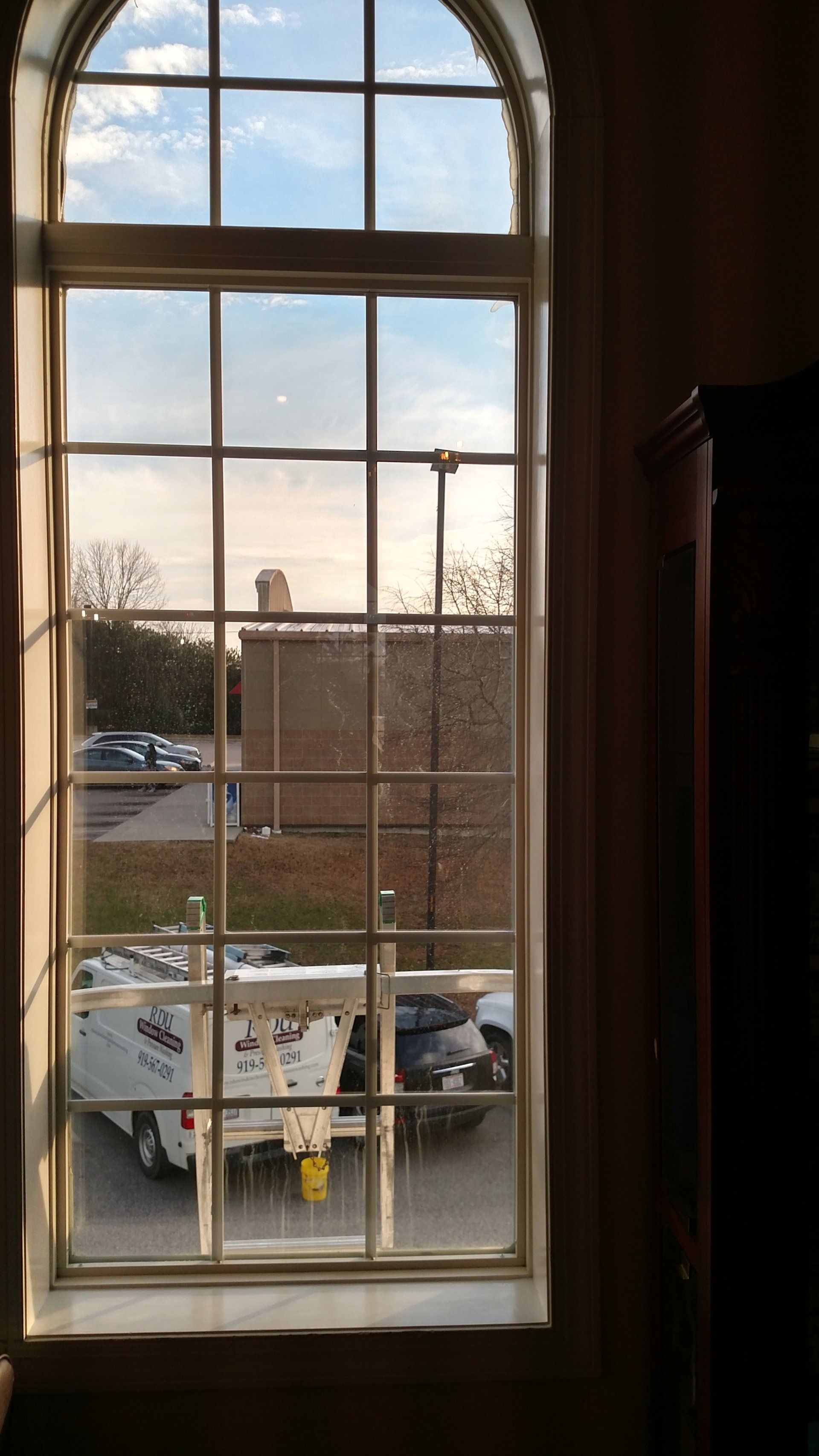 Tall arched window looking onto a patio with a table, chairs, and outdoor view.
