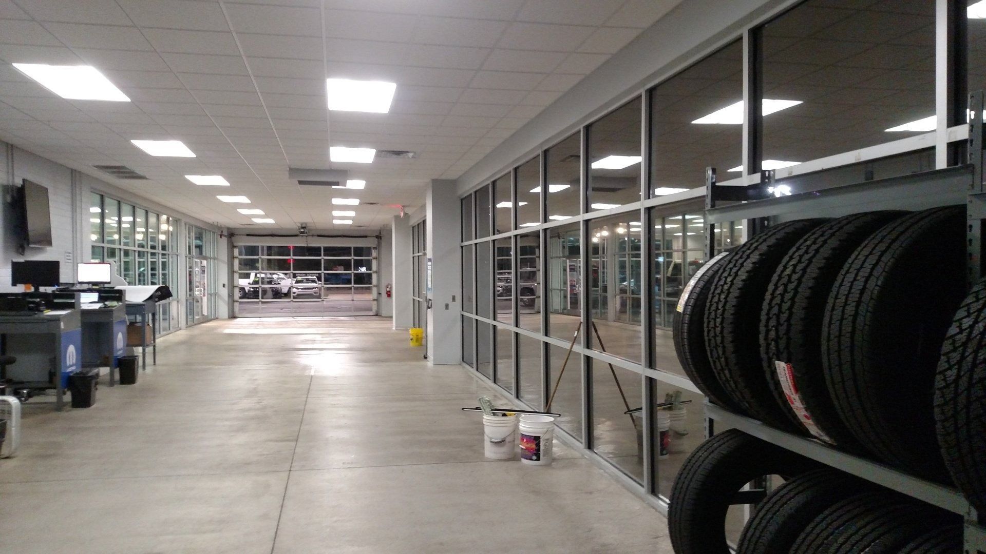 Empty store interior with bright ceiling lights, glass storefronts, and stacked tires along the right wall