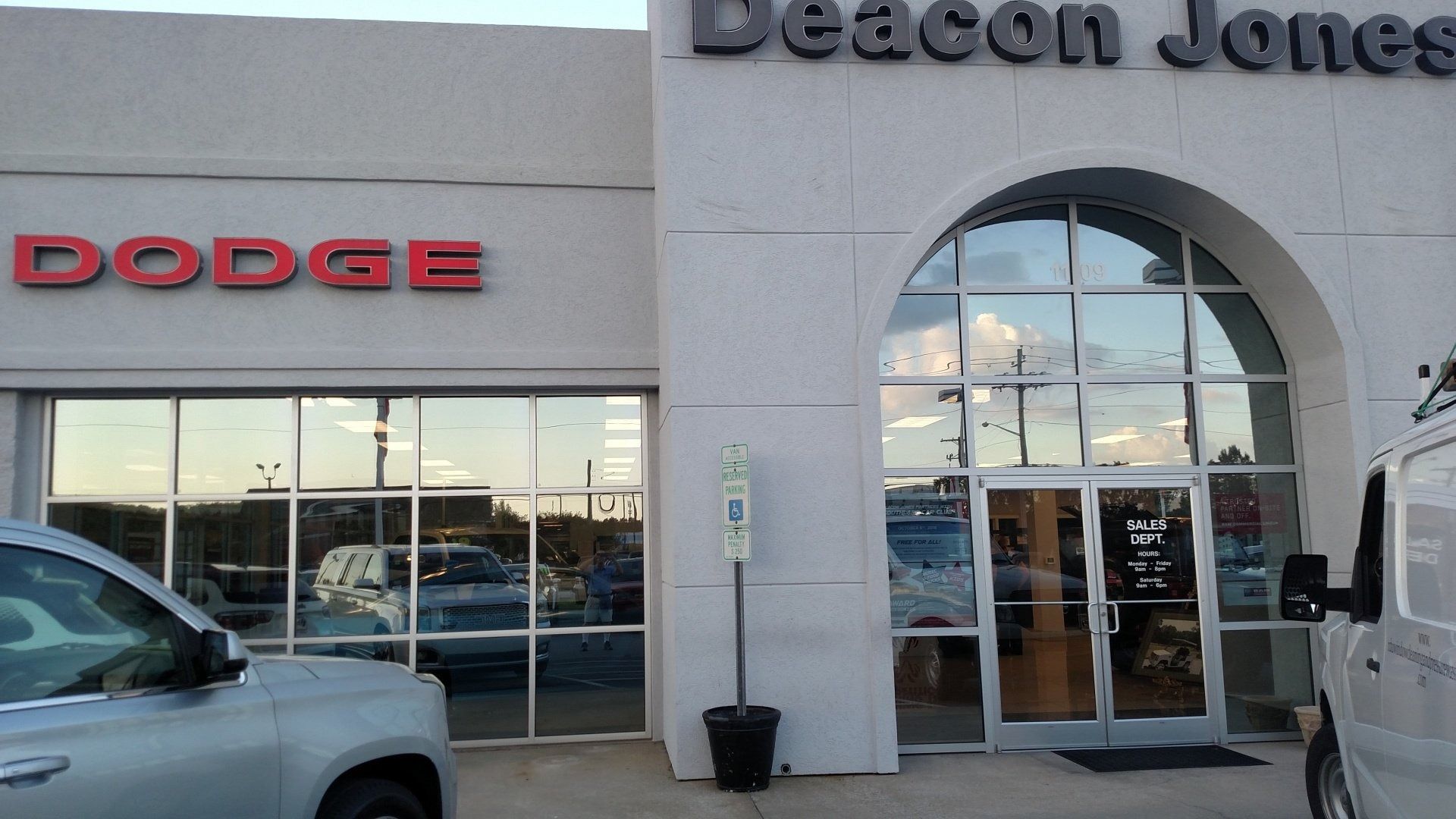 Dodge dealership storefront with glass entrance, parked vehicles, and “Deacon Jones” sign above the doors