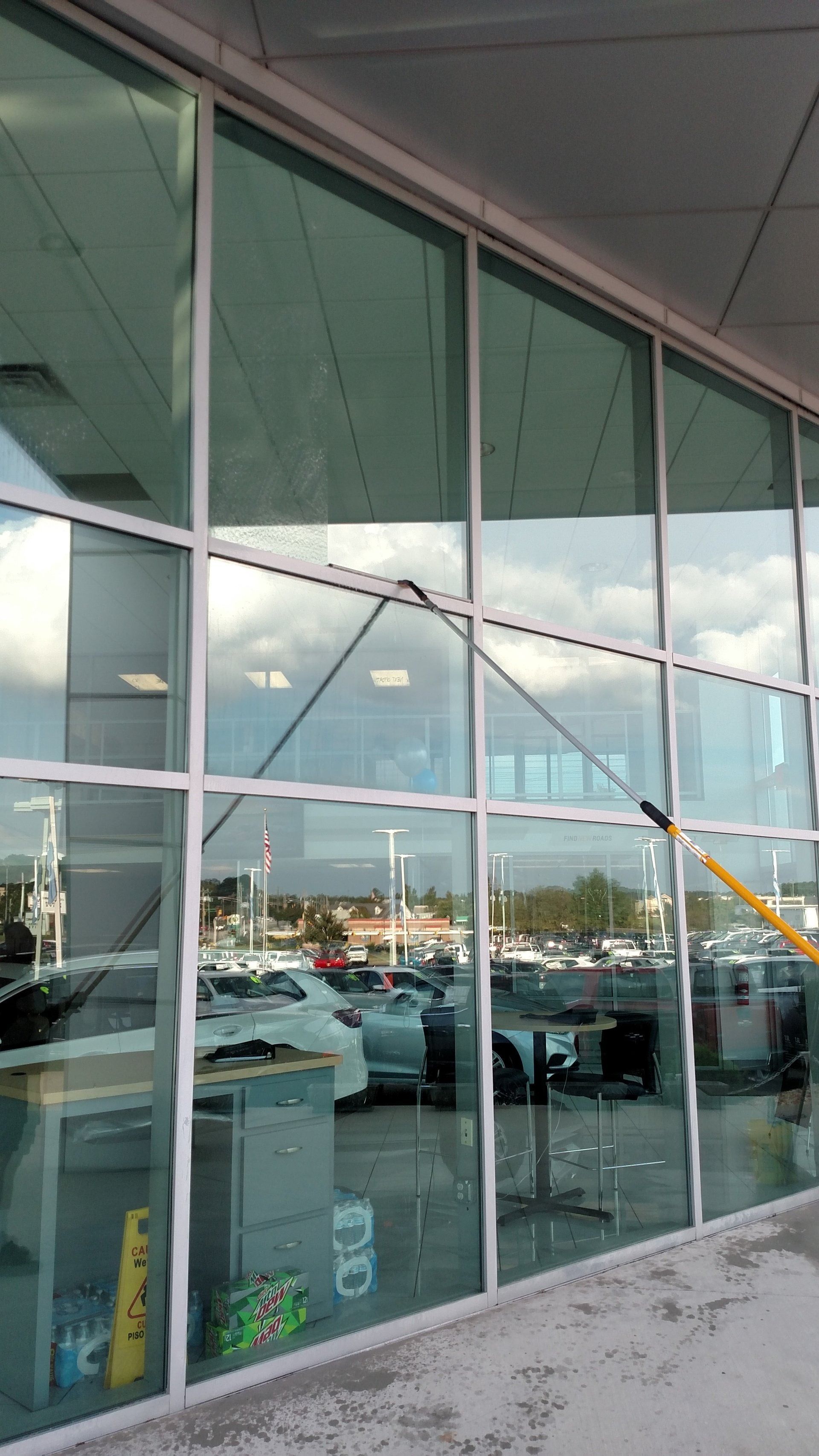 Glass storefront with reflections of parked cars and a yellow barrier outside a building.