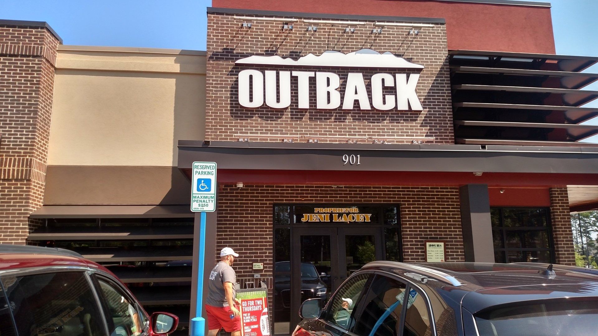 Outback Steakhouse storefront with large sign, parked cars, and a pedestrian entrance.