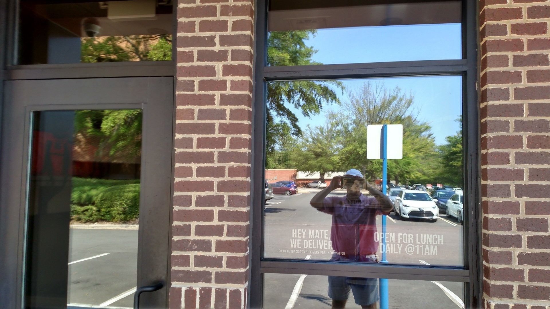 Brick storefront window with a person reflected outside and parked cars across the street.