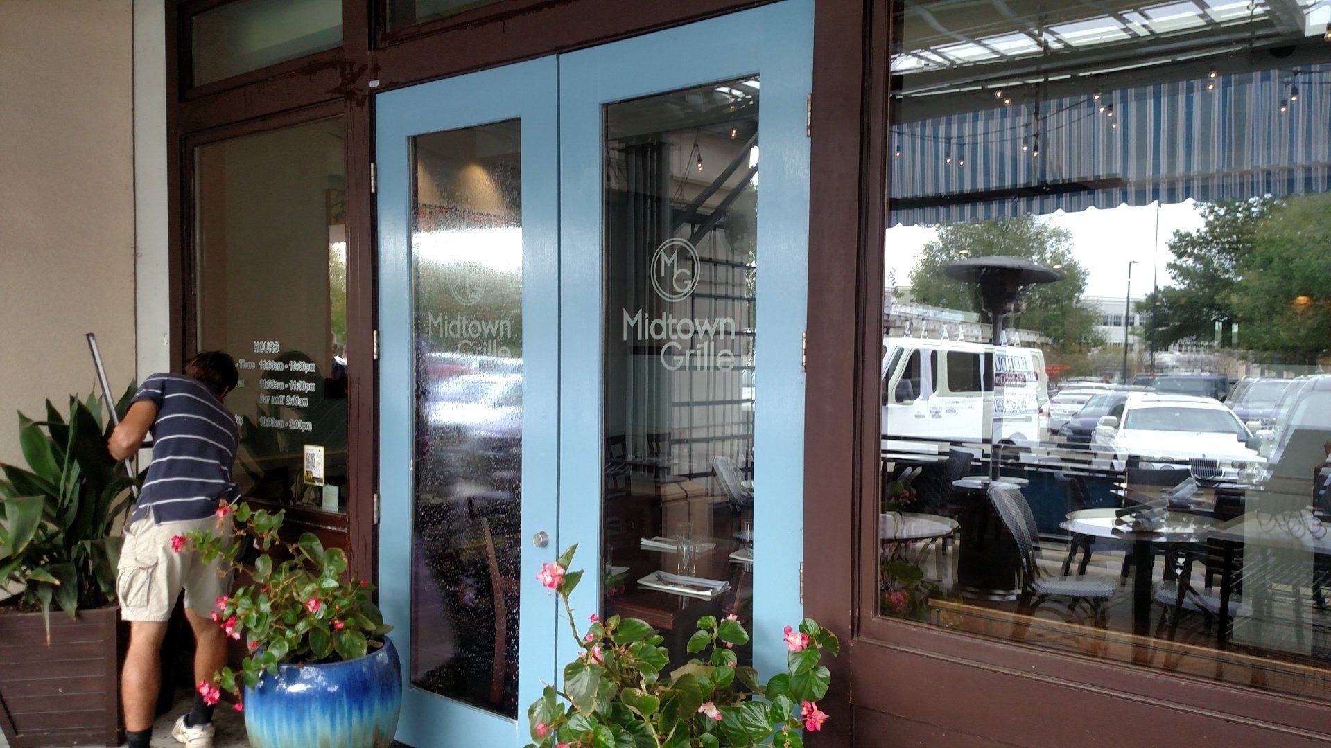Person arranging plants by a glass storefront with tables visible inside.