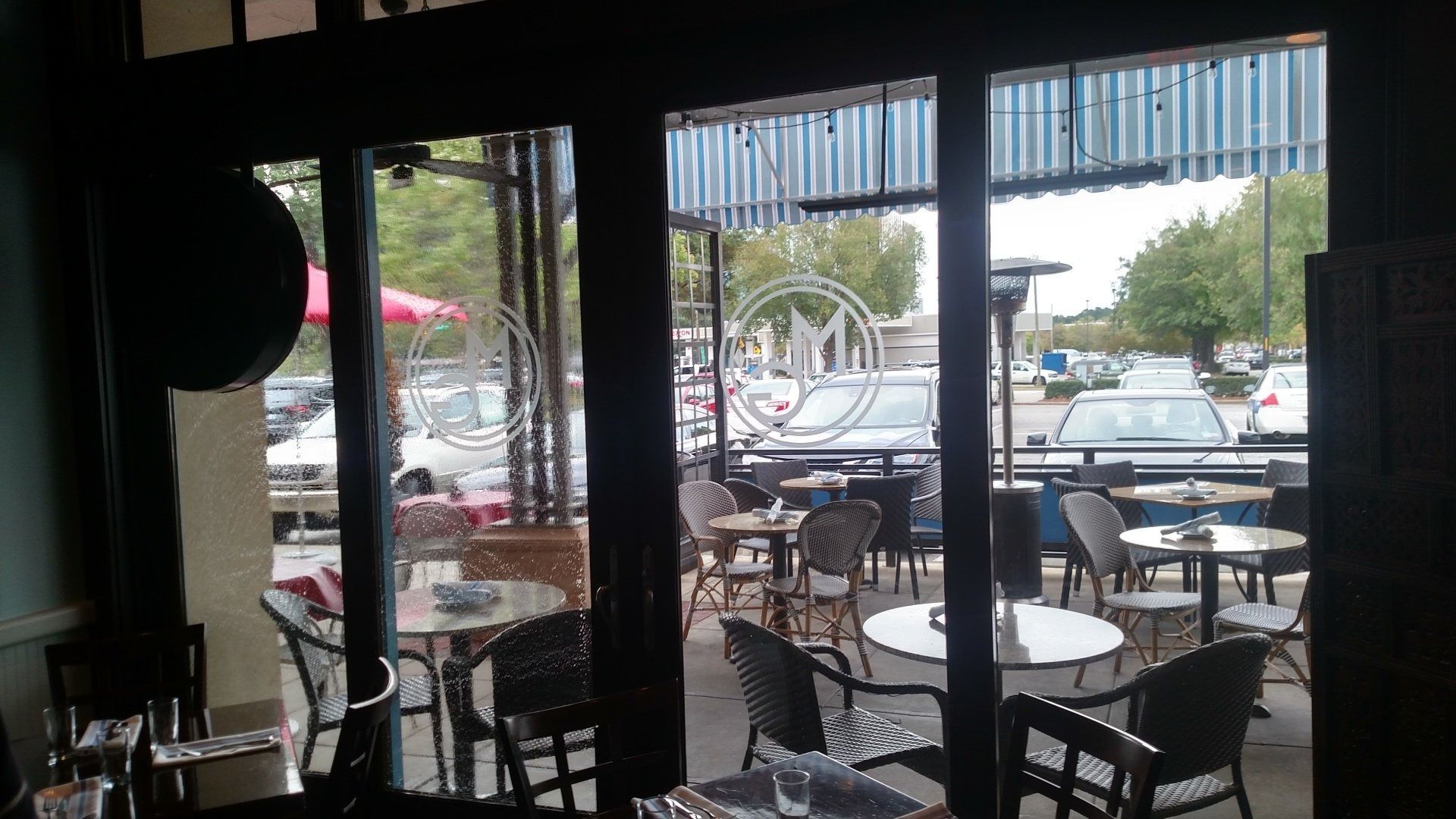Cafe interior looking out to outdoor patio with tables, chairs, and parked cars beyond glass doors