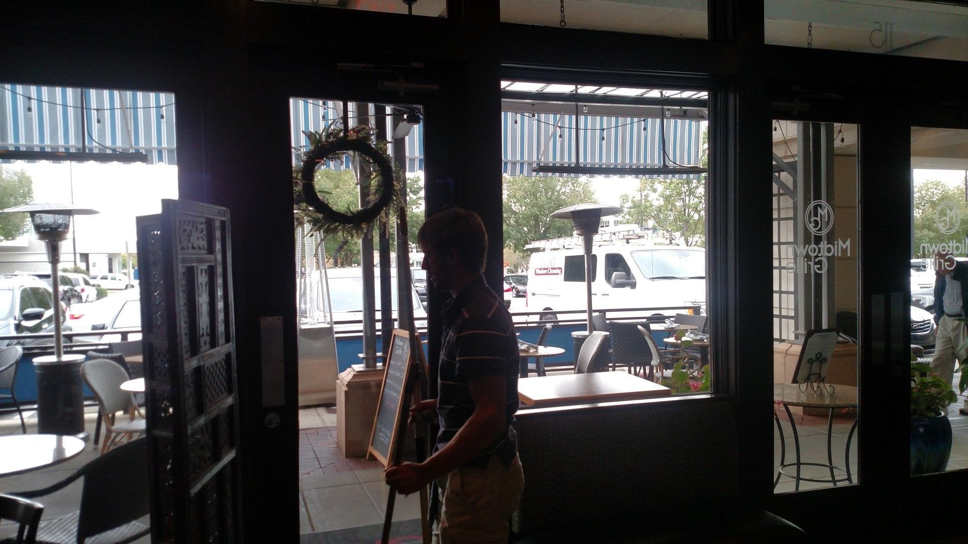 Person standing inside a cafe near the glass entrance, with cars visible outside.