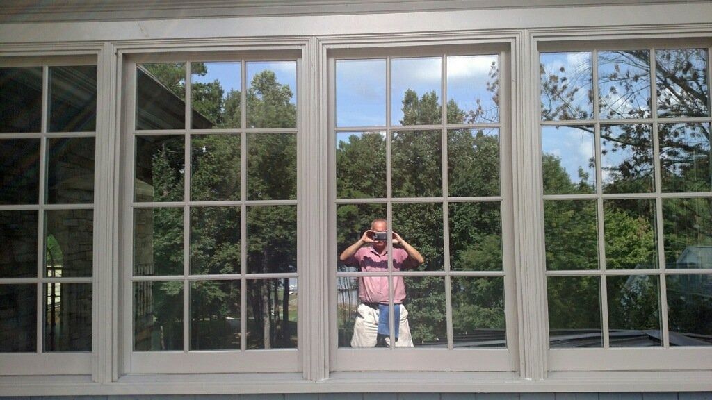 Person in a pink shirt standing behind a large window, reflected in the glass with trees outside.