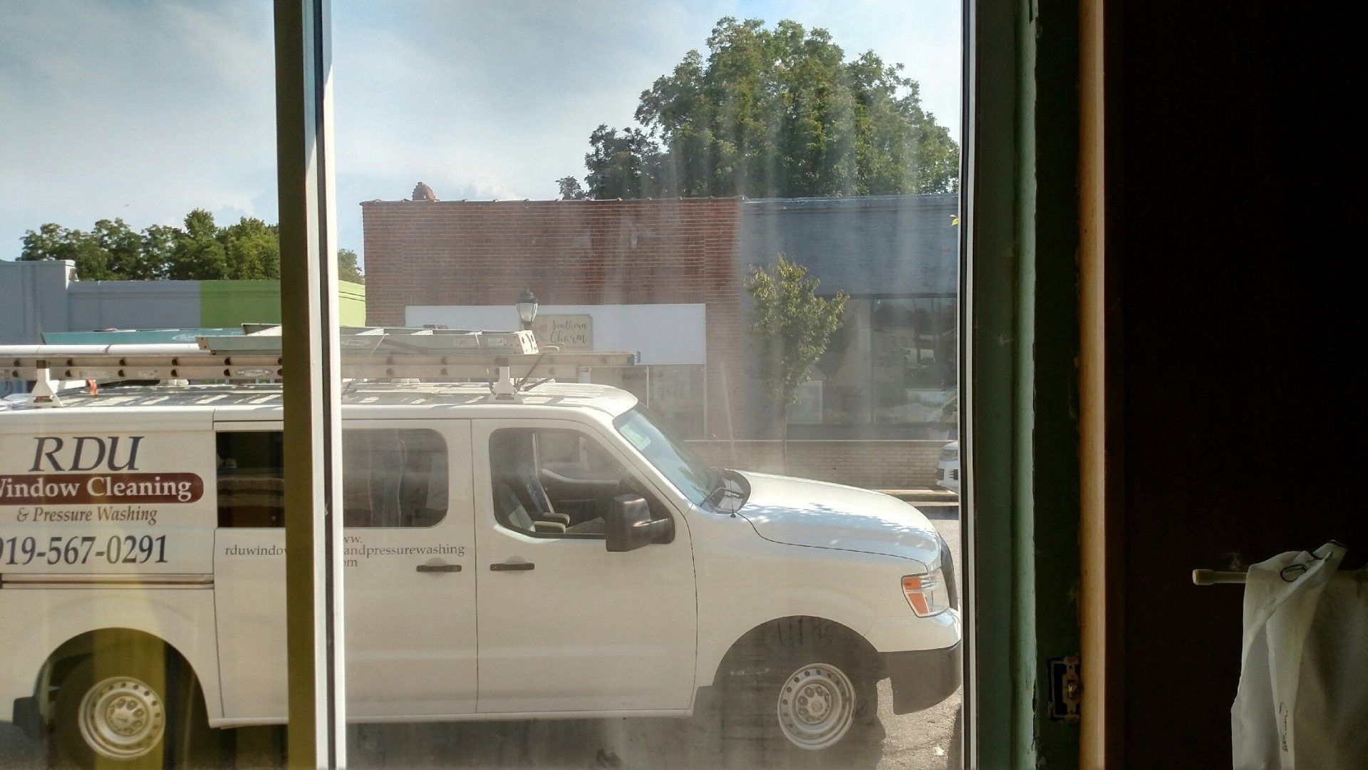 White work van outside a window, with a truck and buildings in the background.
