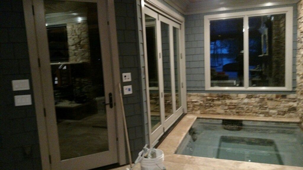 Indoor pool beside glass doors and windows, with stone wall accents and dim lighting.