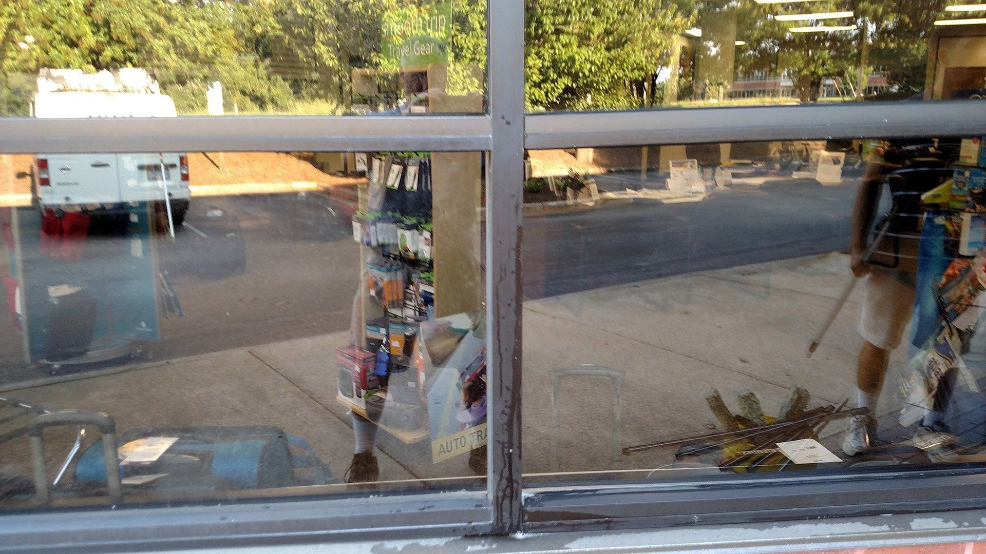 Storefront window reflecting street scene with parked van, trees, and a person standing nearby
