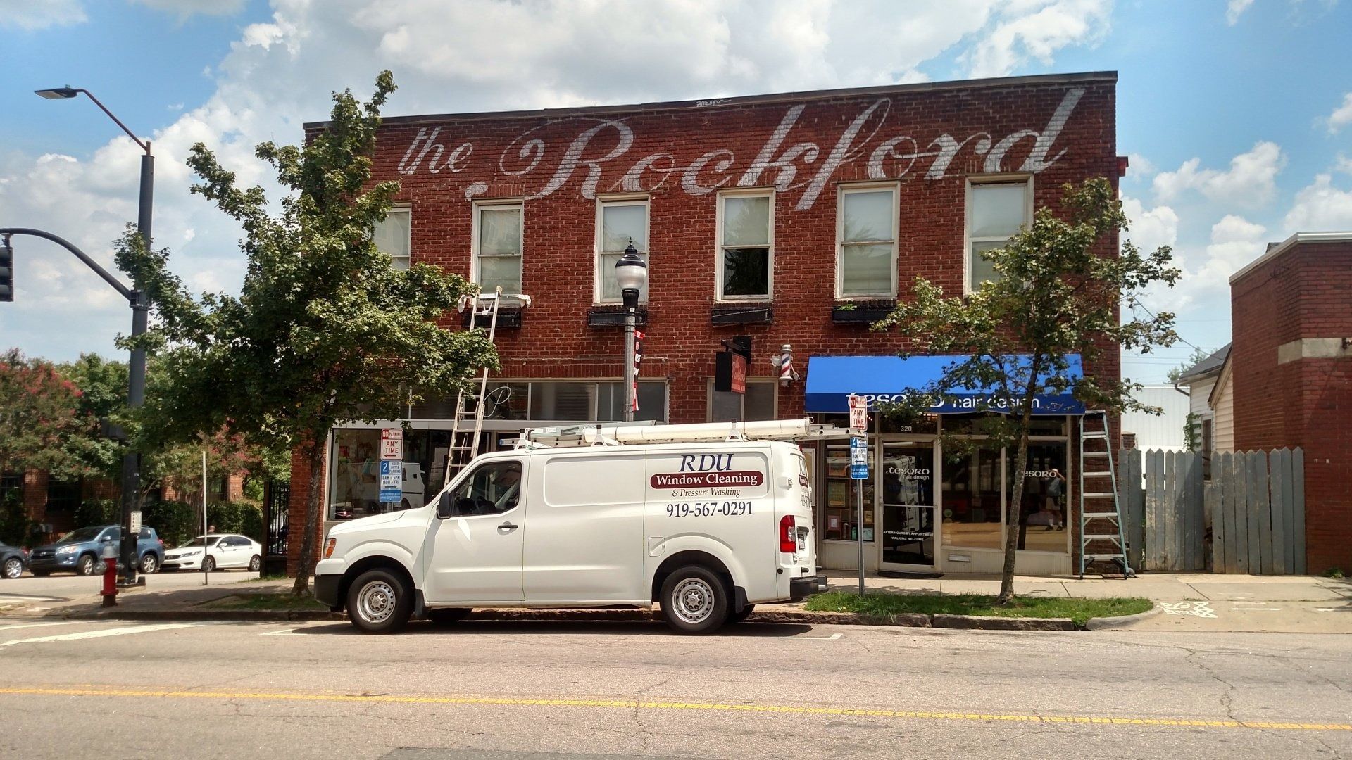 White service van parked in front of a red brick storefront with a large painted mural and blue awning.