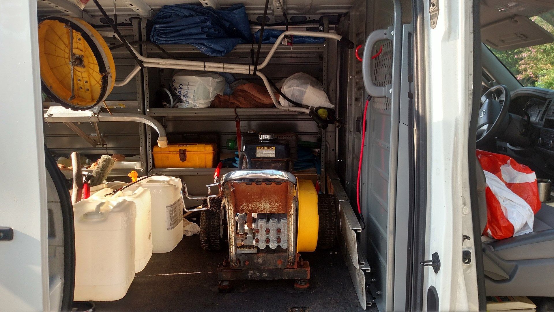 Van interior packed with tools, fuel cans, and a generator, viewed from the open rear doors