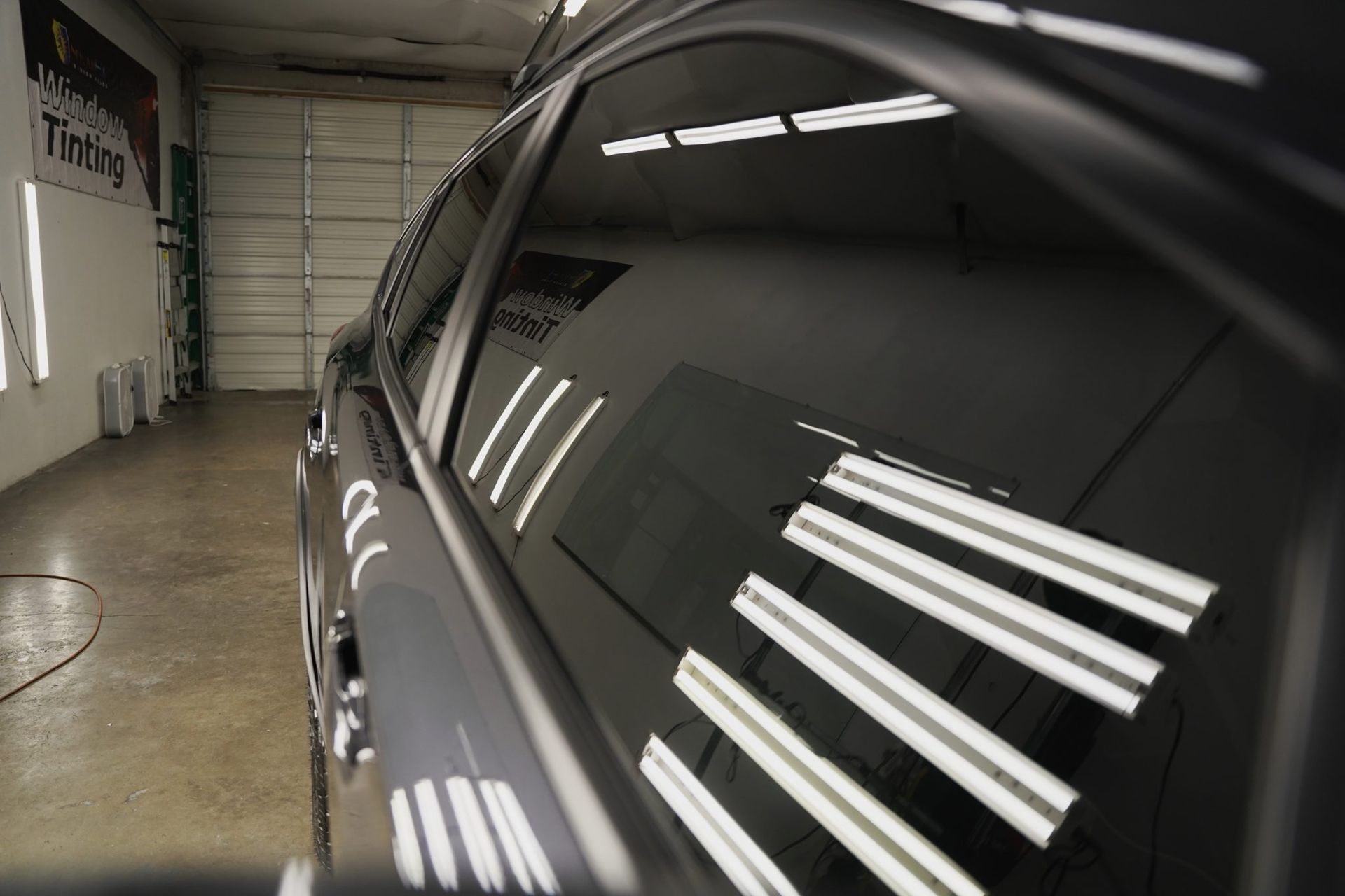 Dark tinted car window reflecting bright, white shop lights.