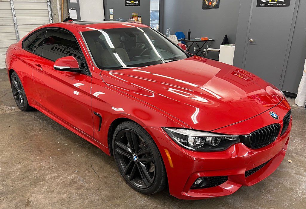 Red BMW coupe with black wheels, tinted windows, parked in a garage.