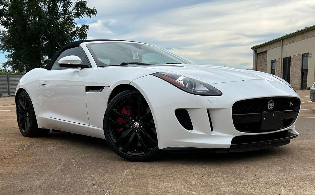 White Jaguar F-Type convertible parked on asphalt. Black wheels, red brake calipers, and a black front grille are visible.