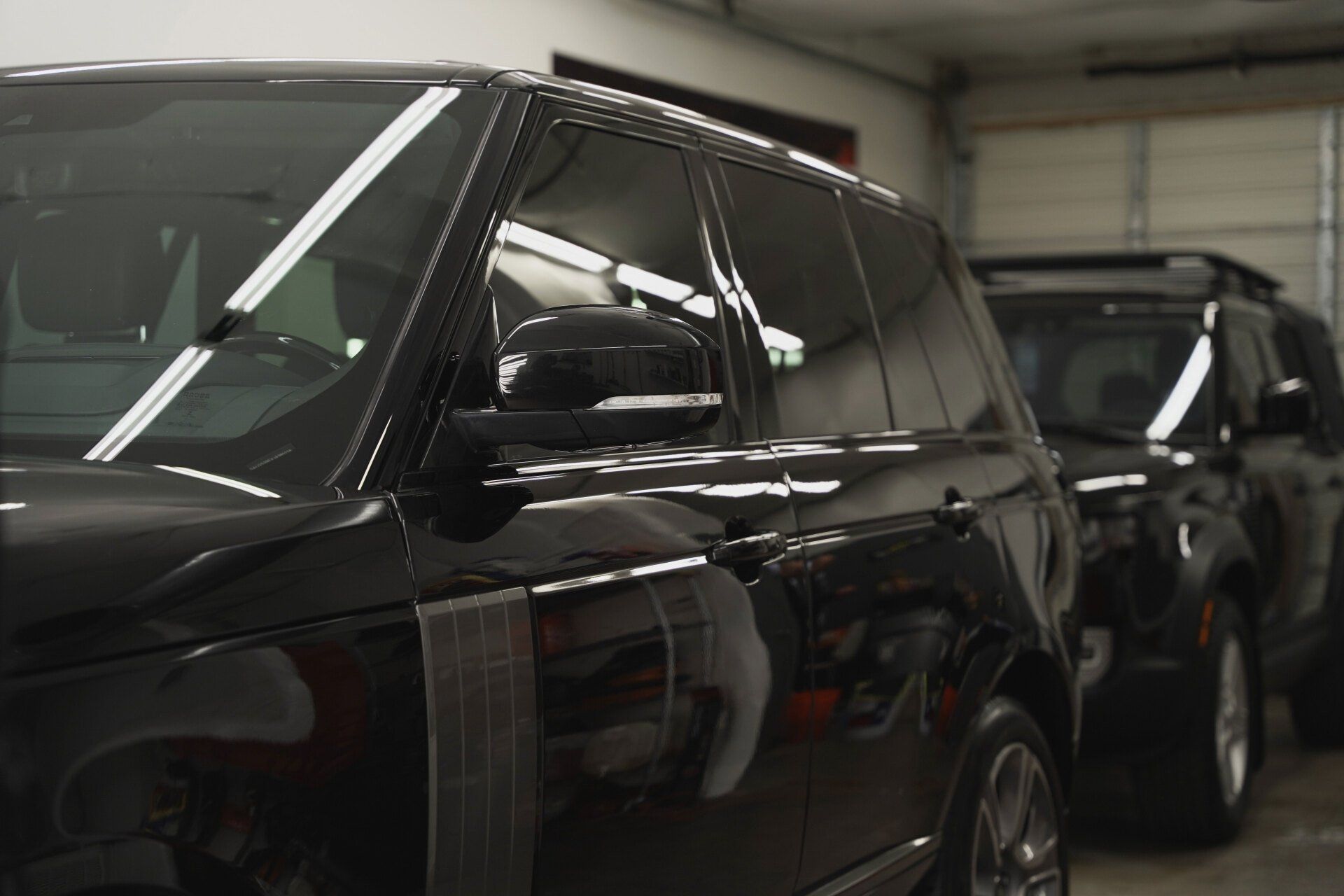 Black SUVs parked inside a well-lit garage, close-up of side panel and windows.