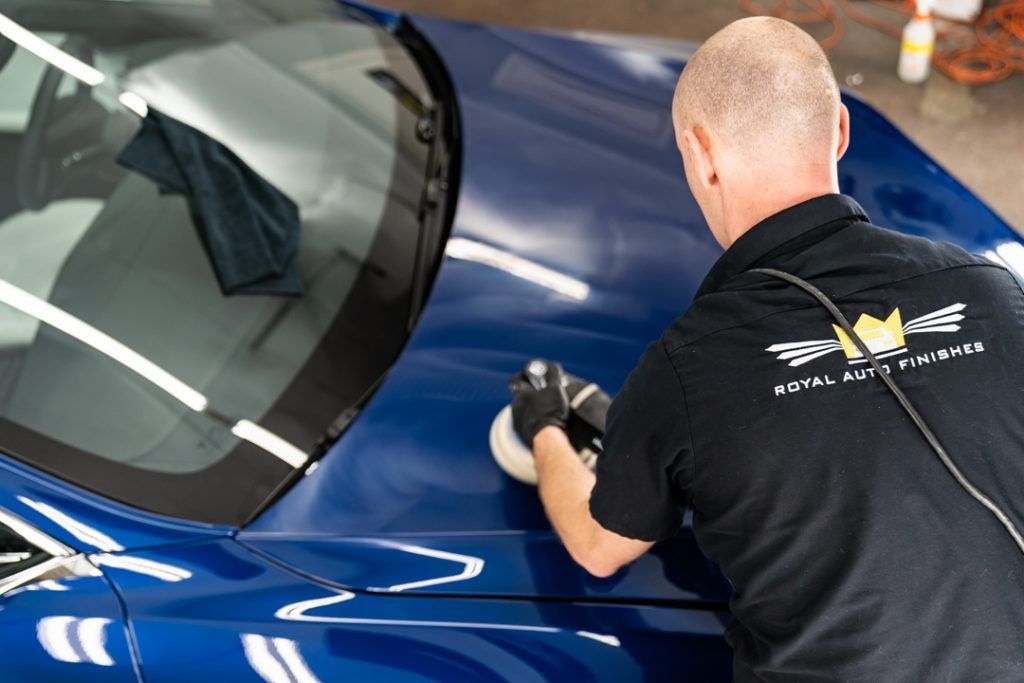 Person polishing a blue car with a buffer in a garage.