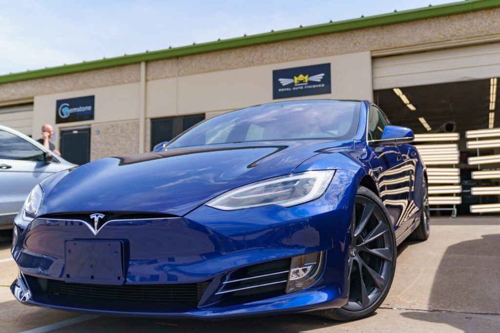 Blue Tesla parked in front of a building with a business sign.
