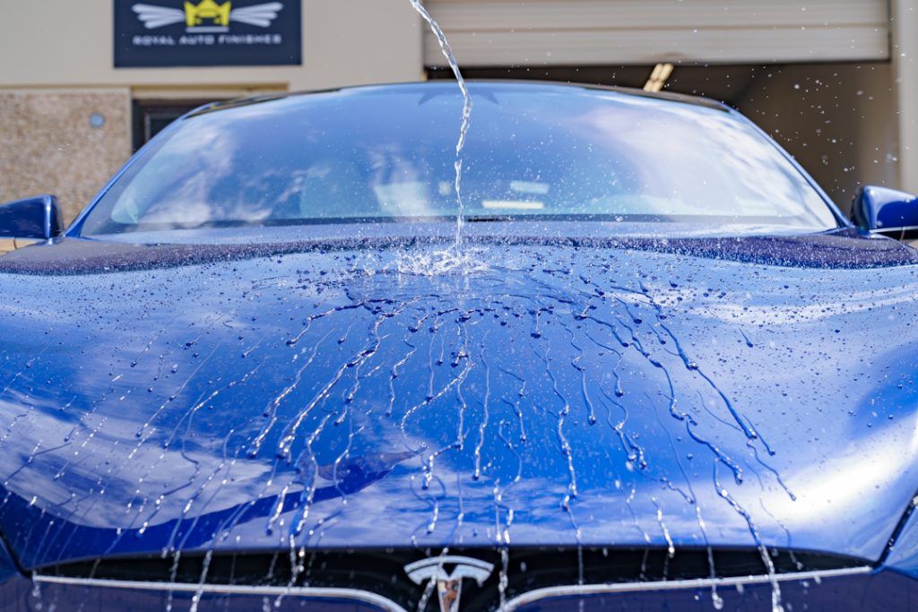 Blue Tesla car being sprayed with water at a car wash.