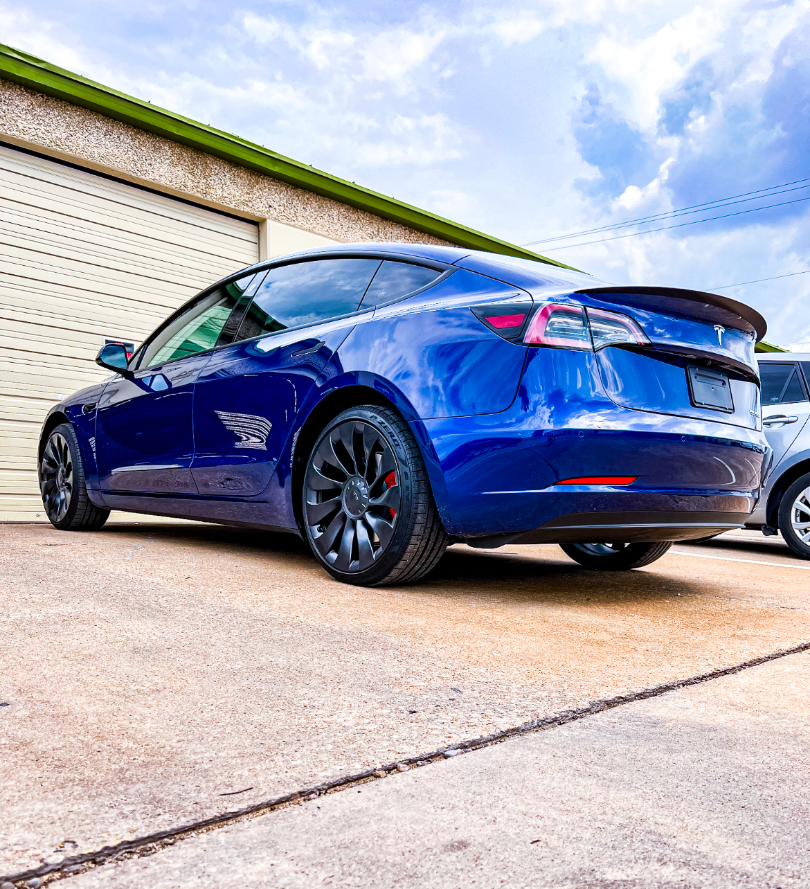 Blue Tesla parked outside a building, black wheels, against a blue sky.