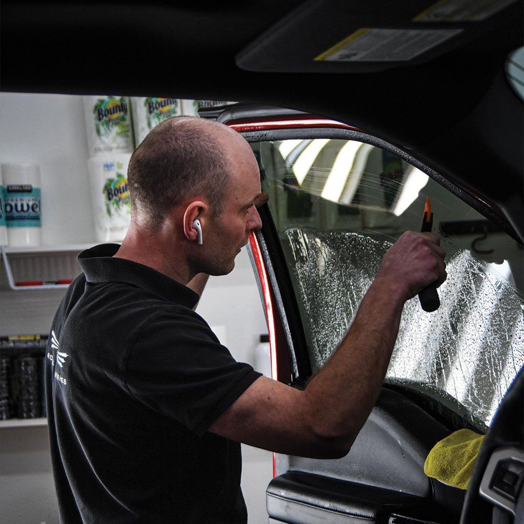 A man applying window tint to a car window. He is using a squeegee tool.