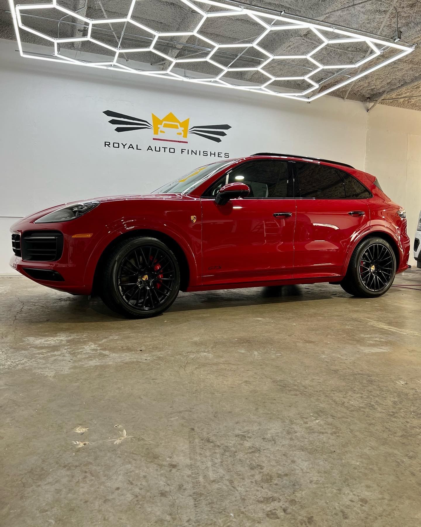 Red Porsche SUV in a well-lit auto shop, black wheels.