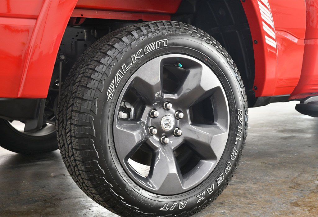 Red pickup truck wheel and tire detail. Gray rim and black tire with white lettering.