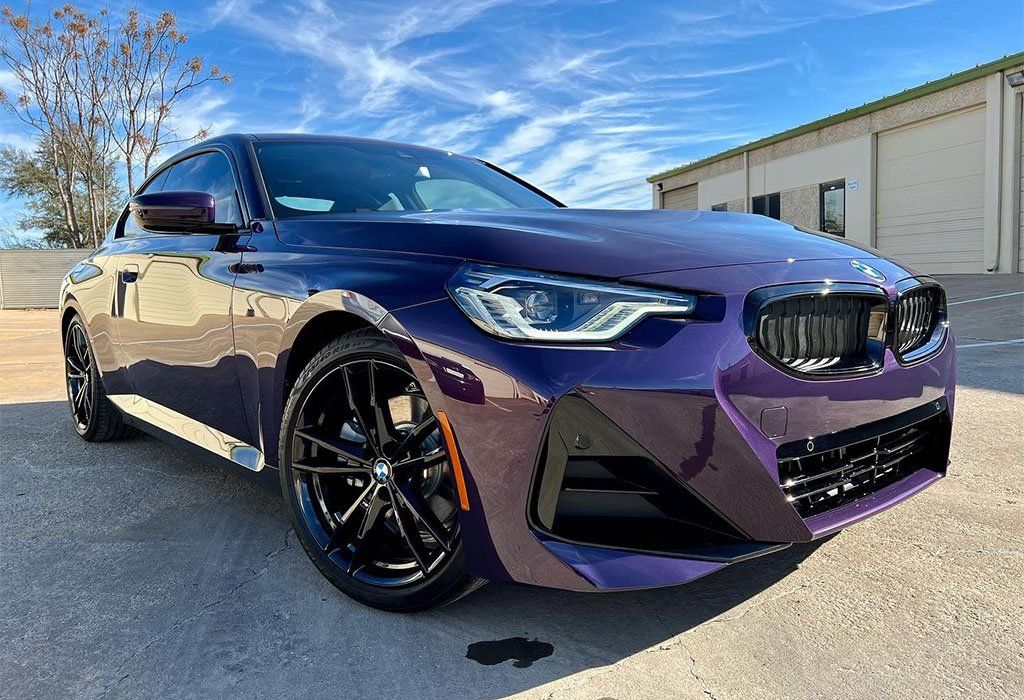 Dark purple BMW sedan parked outdoors on a sunny day. Black wheels.