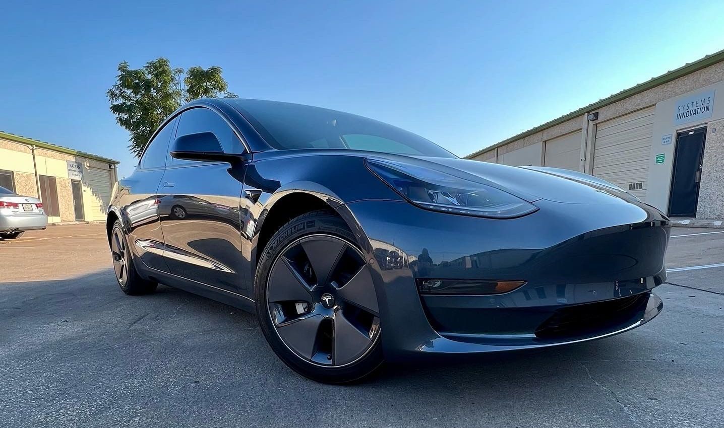 Dark blue Tesla Model 3 car parked outside a building.