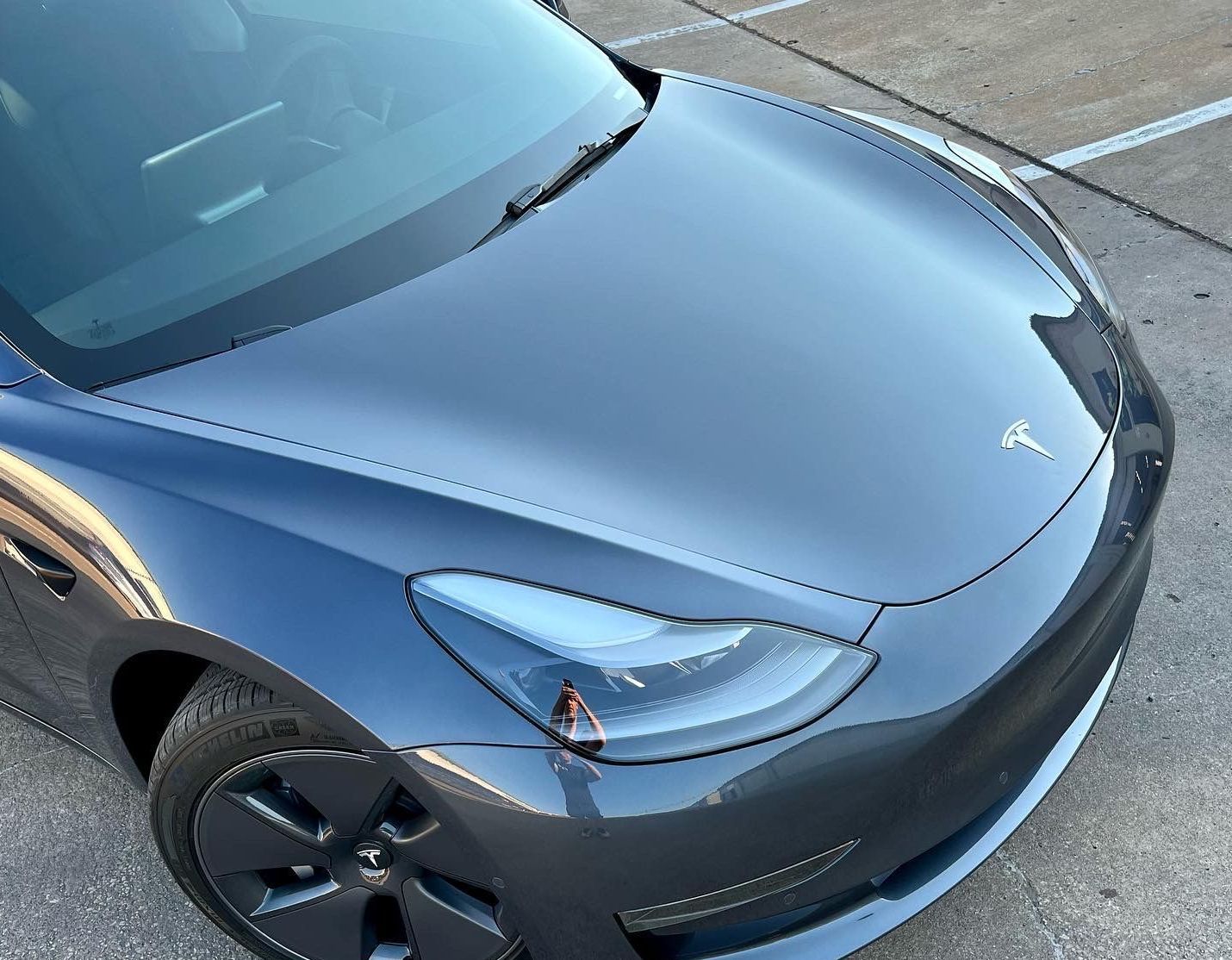 Dark gray Tesla Model 3 car hood and headlights, outdoors.